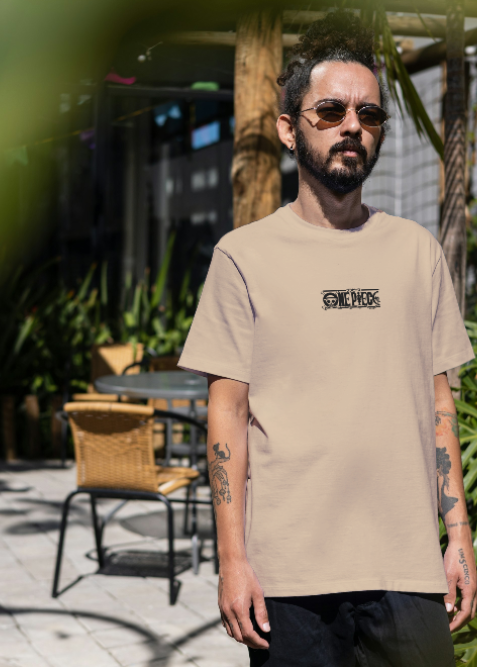 Man wearing a beige t-shirt with text, standing outdoors with greenery around