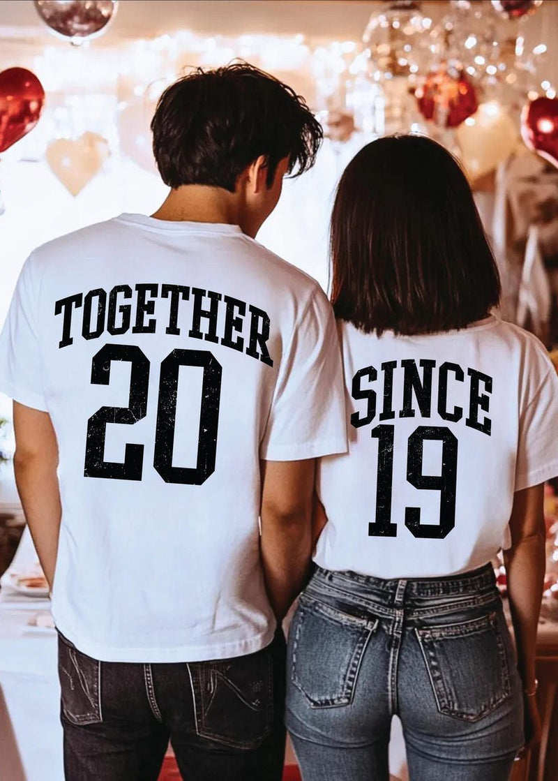 Two people wearing matching shirts with 'TOGETHER 20' and 'SINCE 19' text in a festive setting.
