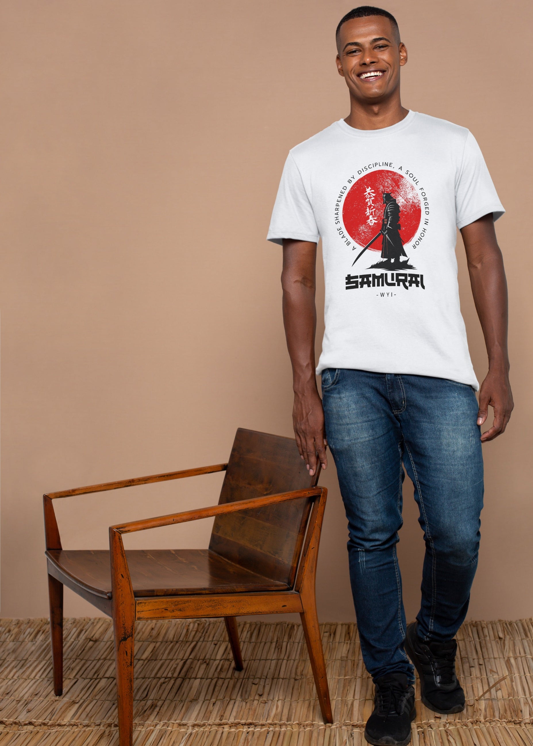 Man wearing a white t-shirt with a graphic design standing next to a wooden chair against a beige wall.