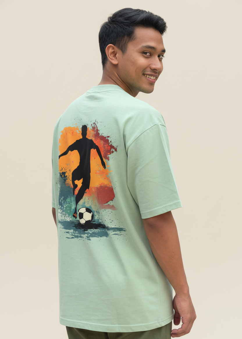 Man wearing a WYI sage green t-shirt with a soccer graphic on the back against a brown background