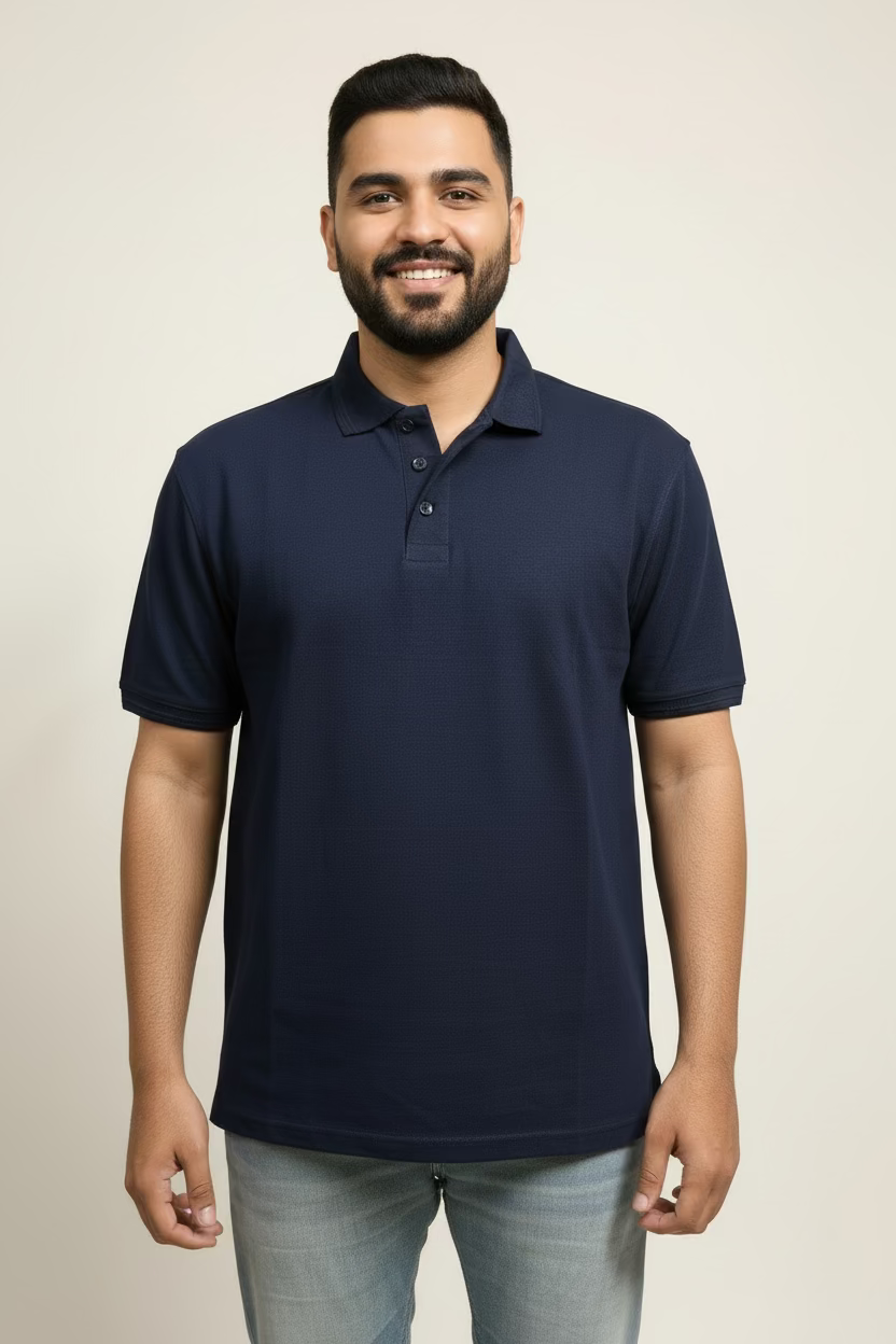 Man wearing a navy blue polo shirt standing in a room with beige walls and wooden paneling.